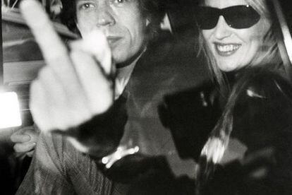 El cantante de los Rolling Stones, Mick Jagger y su entonces esposa, la modelo Jerry Hall se dirigen en coche a la inauguración de la galería Mizuno, en Los Ángeles en enero de 1983. El <i>rolling</i> aparece sacándole el dedo a Galella en protesta porque le fotografiara, cosa que a su mujer sí parece gustarle, por alguna razón, a tenor de la amplia sonrisa que exhibe.