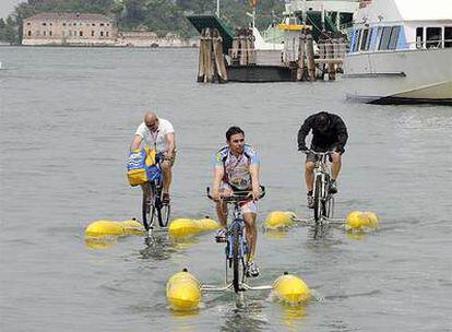 Aficionados montan en bicicleta sobre el agua en el Lido de Venecia, momentos antes del inicio de la primera etapa del Giro.