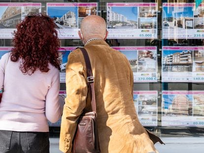 Dos clientes miran los carteles de venta y alquiler de casas en una agencia inmobiliaria de Alicante.
