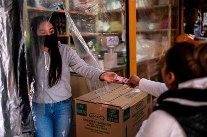 Una vendedora recibe dinero detrás de un plástico en un negocio de México.
