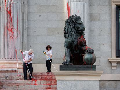 Dos operarias limpian el león del Congreso tras ser pintado por una protesta medioambientalista.