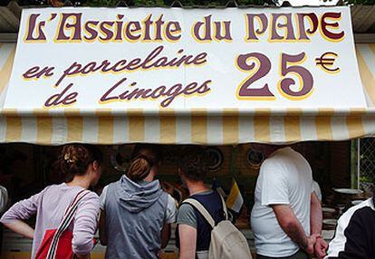 Varios turistas curiosean un puesto en Lourdes que anuncia la venta del plato del Papa en porcelana de Limoges.