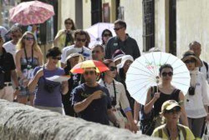 Turistas se protegen del sol con sombrillas y diferentes sombreros durante su paso por la Carrera del Darro en Granada.