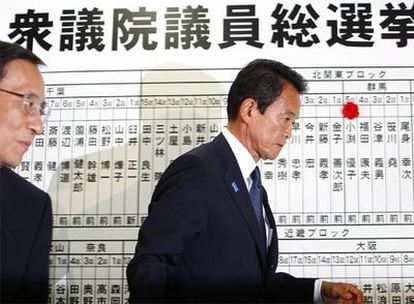 El primer ministro japonés, Taro Aso (derecha), abandona la sede de su partido en Tokio ante el cartel donde se marcan, con una rosa artificial, los escaños obtenidos.
