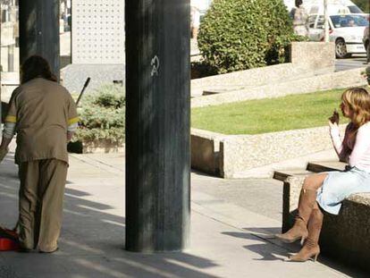 Una limpiadora recoge colillas mientras otra mujer fuma en la vía pública en Madrid.