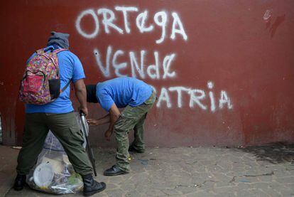 Paramilitaries limpian el suelo frente a un rayado en el que se lee: 