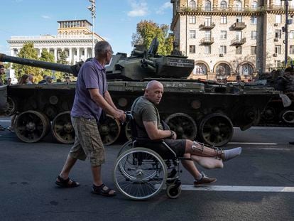 Un hombre empuja la silla de ruedas de un militar ucranio frente a un tanque ruso destruido expuesto en el centro de Kiev, durante los festejos del Día de la Independencia, este jueves 24 de agosto.