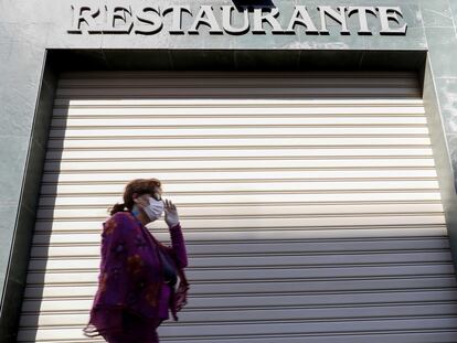 Una persona con mascarilla pasa delante de un restaurantes cerrado en Valencia.