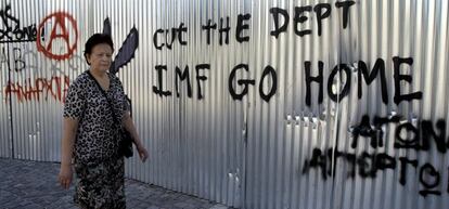 Una mujer camina junto a un grafiti en el que se puede leer "FMI vete a casa, corta la deuda" en Atenas.