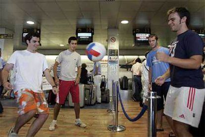 Cuatro pasajeros juegan al fútbol junto a puestos de facturación de Iberia en el aeropuerto de El Prat.