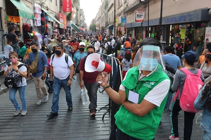 Un funcionario promueve el distanciamiento social en una concurrida calle comercial del centro histórico de la Ciudad de México.