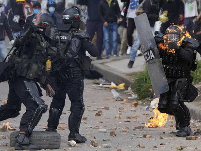 Dos policías corren para ayudar a un compañero que fue alcanzado con una bomba de gasolina durante una protesta en Bogotá, Colombia.