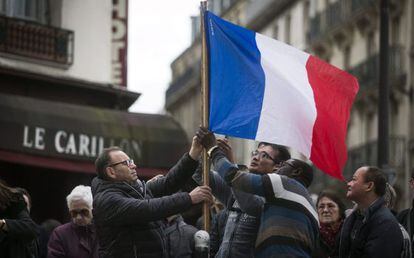 Tres persones col·loquen una bandera francesa a París.