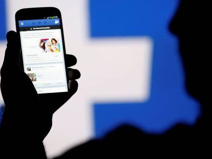 Una persona consulta su teléfono móvil delante de un logotipo de Facebook.