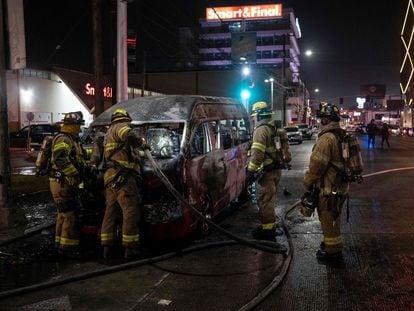 Bomberos trabajan alrededor de un vehículo de transporte público que fue incendiado, la noche del viernes, en Tijuana.