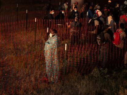 Un migrante, cubierto con una manta, mira hacia un campo que conduce a la frontera con México mientras él y otros esperan subir a un autobús de Aduanas y Protección Fronteriza en Del Rio, Texas.