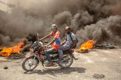 Aunado al conflicto entre pandillas, las calles de la capital haitiana han sido tomadas por grupos de manifestantes que reclaman un alza al salario mínimo y un abasto efectivo de combustibles. En la imagen, dos hombres circulan alrededor de barricadas incendiadas durante un protesta en Puerto Príncipe, el 13 de julio de 2022. 