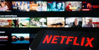 Logo de Netflix en un móvil con imágenes de películas y series de fondo.