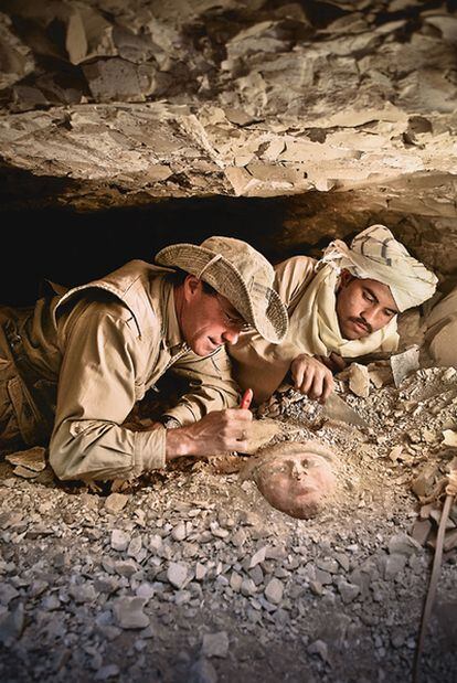 El egiptólogo José Manuel Galán desentierra, junto al trabajador especializado Omar Farouk, una máscara de ataúd en un pozo funerario.