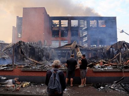 Tres ciudadanos miran este viernes los restos de un edificio en Roubaix, de la empresa Tessi, que fue quemado la tercera noche de disturbios en Francia originados tras la muerte de un menor de 17 años a manos de la policía.