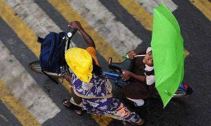 Una niña india sostiene un paraguas mientras se sienta en una bicicleta al cruzar una carretera durante las lluvias fuertes en Chennai.