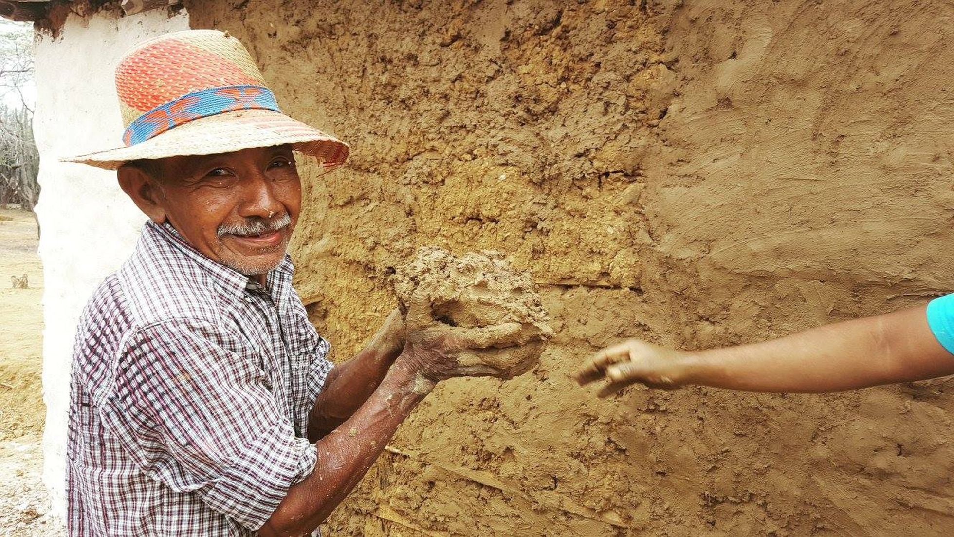 Un hombre construye una casa con barro en la zona desértica de la Guajira.