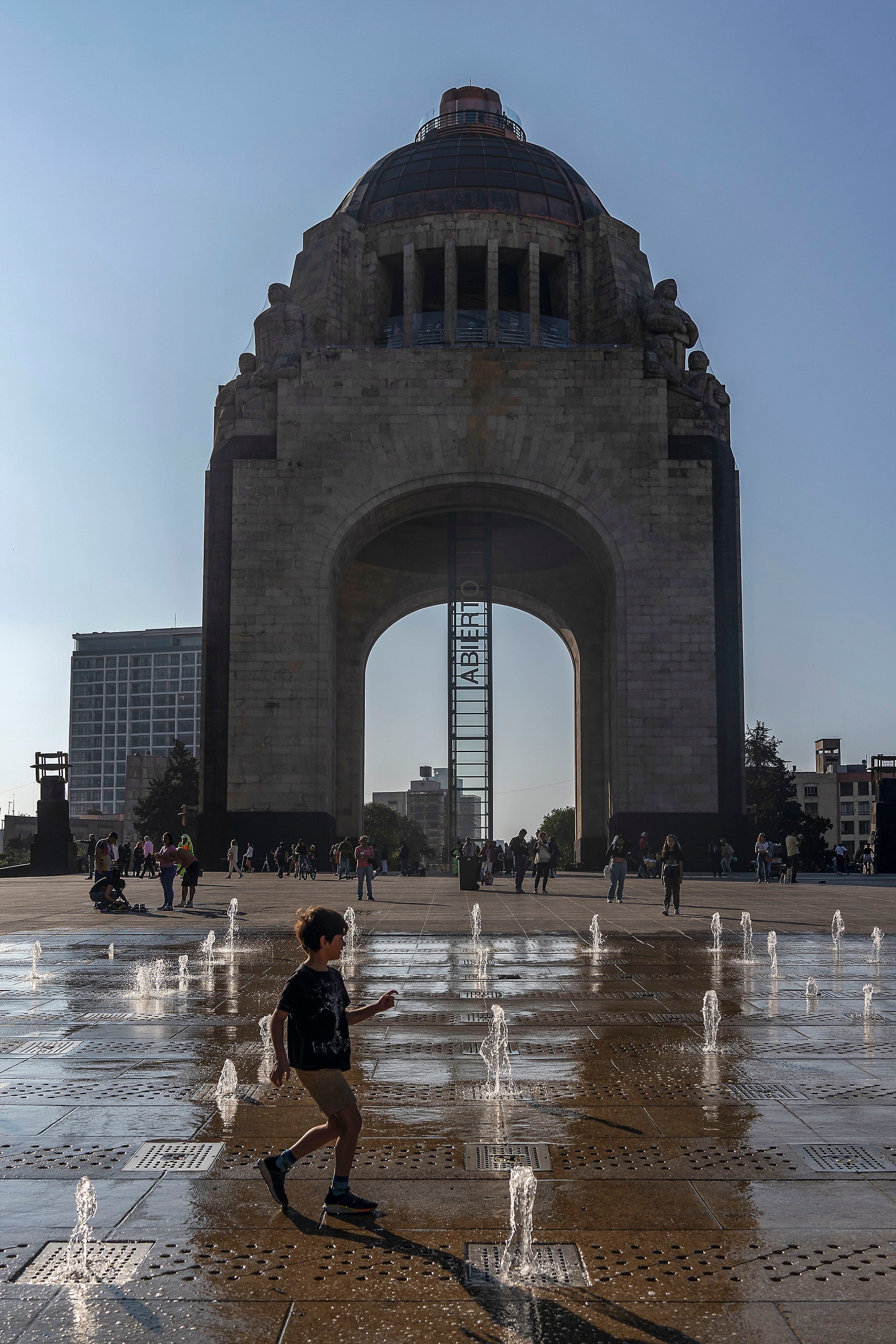 Transeúntes juegan en las fuentes del Monumento a la Revolución.