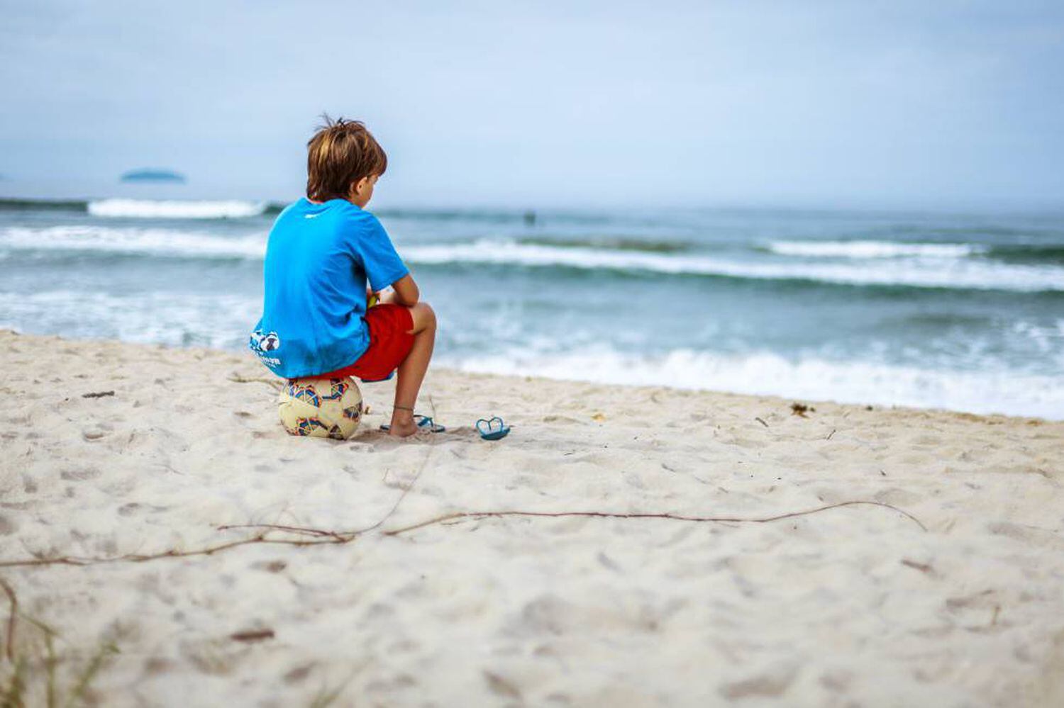 Un niño está sentado en la playa, mirando el mar.
