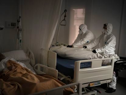 Los trabajadores de una funeraria trasladan a un fallecido por coronavirus en una residencia de mayores de Barcelona mientras otro anciano duerme.