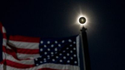 Un eclipse solar total se ve junto a una bandera estadounidense ondeando en Houlton, Maine, EE.UU. 8 de abril de 2024.