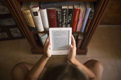 Una noia llegeix un 'e-book' junt amb diversos llibres.