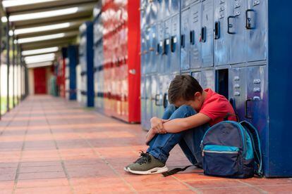 Un niño llora en el suelo del pasillo de un colegio. 