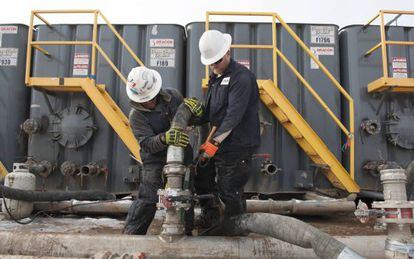 Dos trabajadores conectan mangueras a una tubería en Dakota del Norte.