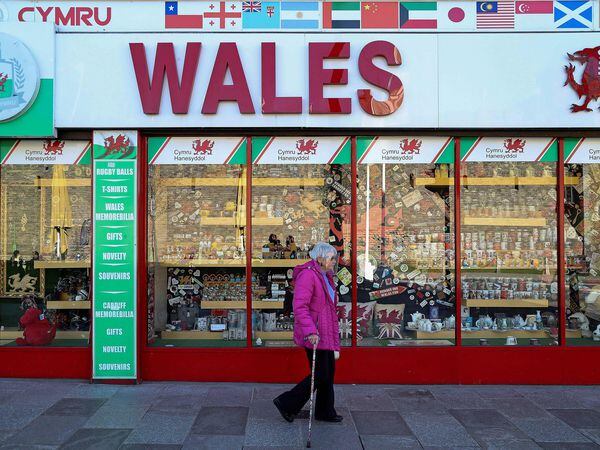 (FILES) In this file photo taken on September 27, 2020 a woman wearing a protective face visor walks past a souvenir shop selling Welsh-themed items, in Cardiff, south Wales. - Wales will impose a full "firebreak" lockdown for two weeks from October 23, to try to reduce a soaring number of new coronavirus cases, First Minister Mark Drakeford said on October 19, 2020. Under the new rules, everyone will be required to stay at home with only critical workers expected to go to their workplaces. (Photo by Geoff Caddick / AFP)