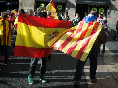 Un ciudadano con una bandera estelada colgada del cuello cruza la plaza Sant Jaume junto a otras personas que portan banderas españolas, en Barcelona.