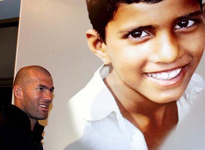 Zinedine Zidane pasa pordelante del poster de un niño sin hogar