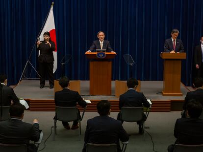 El primer ministro japonés Yoshihide Suga, en el centro, y el responsable del gobierno japonés sobre la pandemia, Shigeru Omi, a la derecha, en una rueda de prensa para actualizar los datos de contagios y medidas en el país nipón