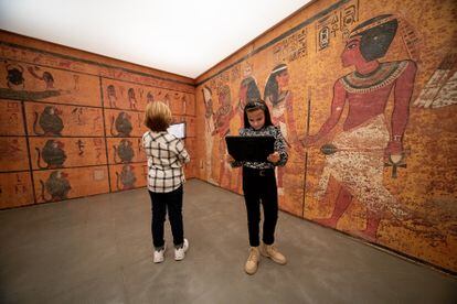 Un niño y una niña recorren la reproducción a tamaño real de la tumba de Tutankamón con unas tabletas.