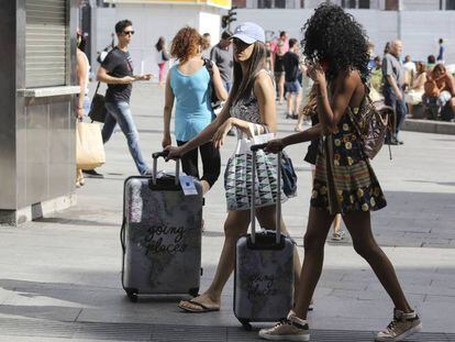Dos jóvenes turistas camino de sus hospedajes en el centro de Madrid, con sus maletas caminando por la Puerta del Sol