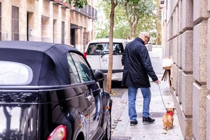 Un hombre camina con su perro por una acera estrecha del centro de Madrid, con coches aparcados. 