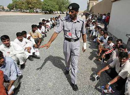 Un policía obliga a colocarse en el suelo a trabajadores, la mayoría asiáticos, que hacen cola frente a la oficina de inmigración de Dubai.