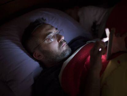Un hombre consulta su móvil en la cama.