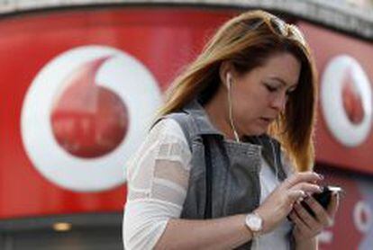 Una mujer habla por un m&oacute;vil mientras pasean junto a una tienda de Vodafone.