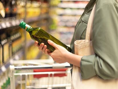 Una mujer compra una botella de aceite de oliva en un supermercado.