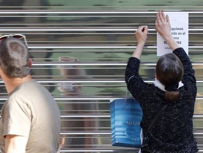 Una mujer coloca un aviso en la persiana cerrada de un negocio del centro de Oviedo.