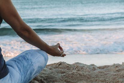 Una persona medita junto a la orilla del mar.