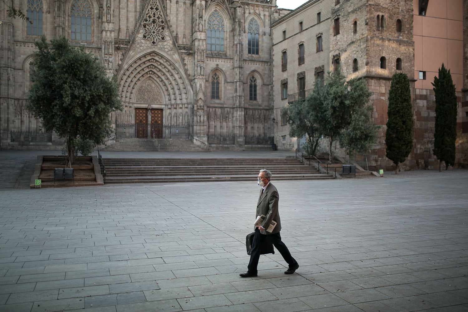 Un hombre camina con mascarilla y maletín mujer por la Avenida de la Catedral en Barcelona