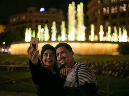 Una pareja se fotograf&iacute;a ante las fuentes gemelas de Plaza Catalu&ntilde;a, en Barcelona, iluminadas de amarillo en solidaridad con los presos.