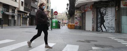 Una mujer protegida con una mascarilla camina por una calle vacía.