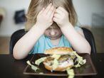 Una niña no quiere comer una hamburguesa.